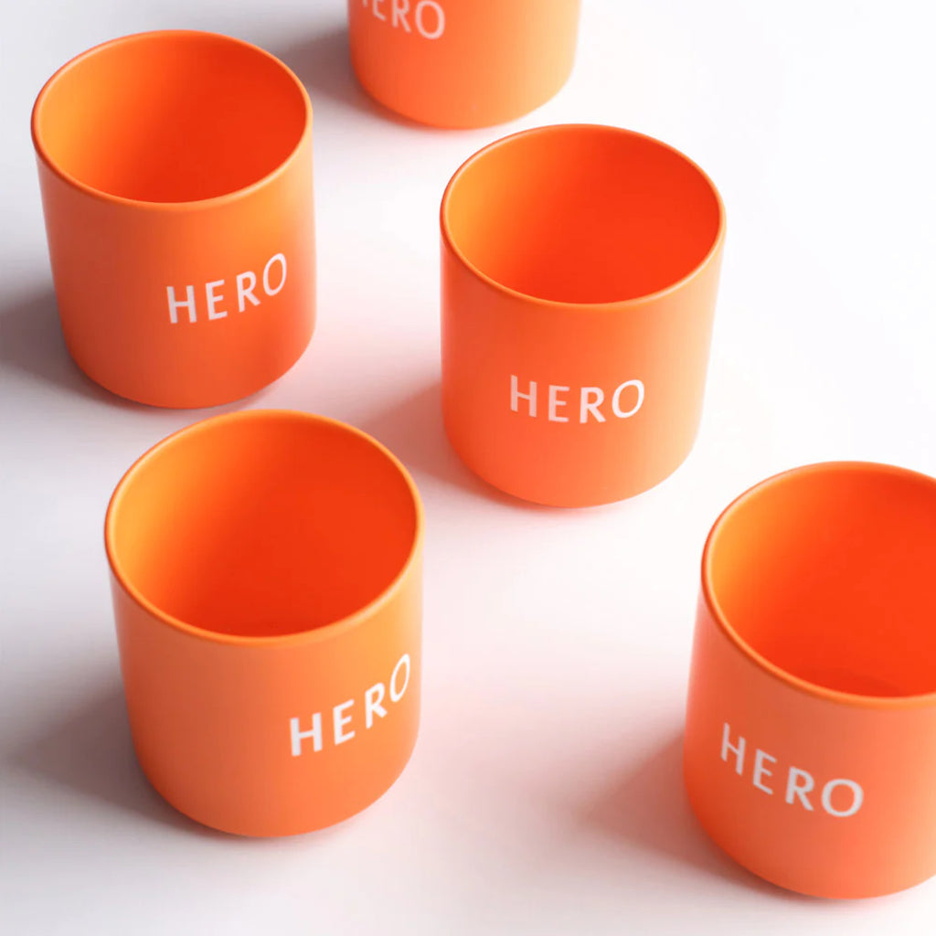 Mehrere Tassen in orange mit Schriftzug HERO auf einem Tisch dekoriert