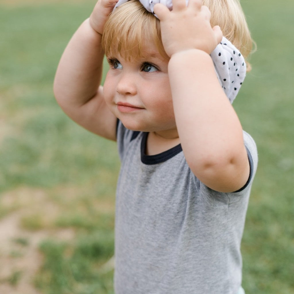 Ein Kleinkind trägt ein Musselintuch weiß mit schwarzen Punkten als Stirnband