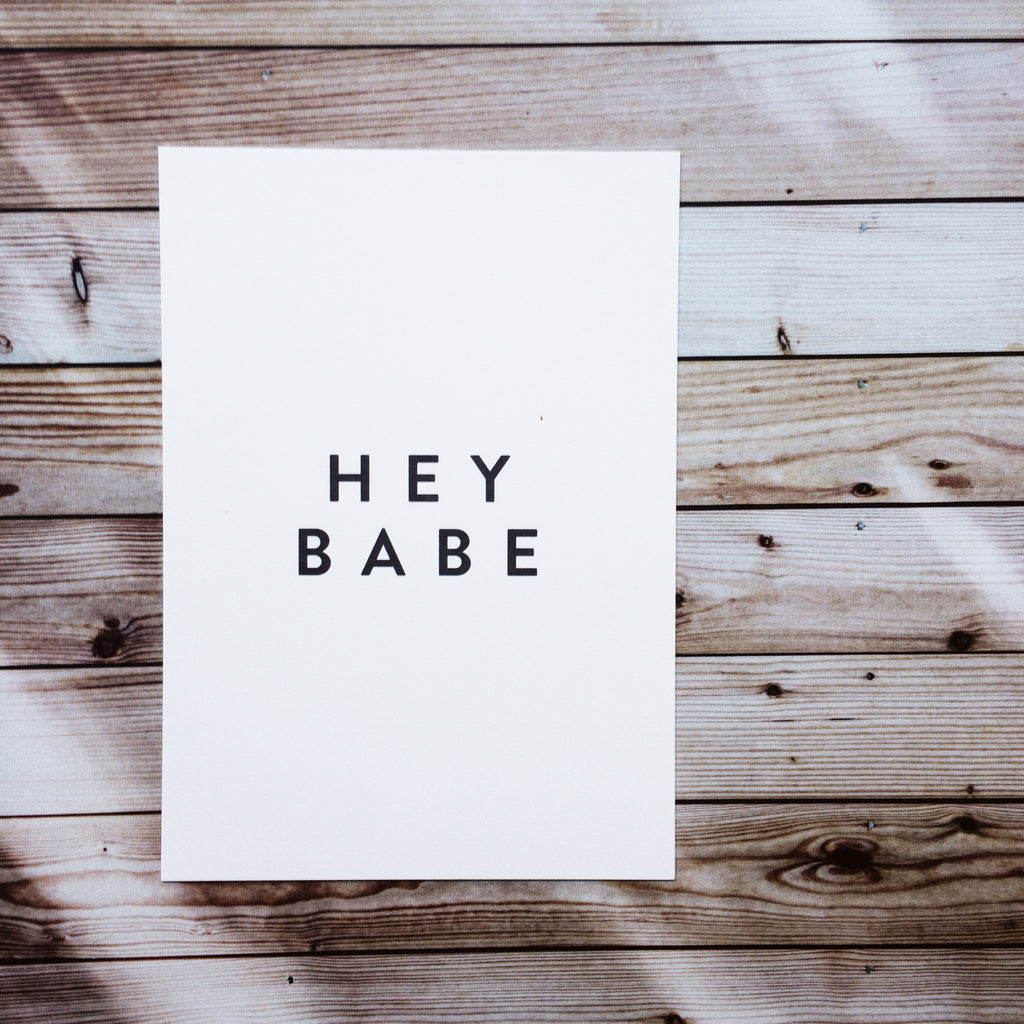 Weiße Postkarte mit schwarzer Schrift "Hey Babe"