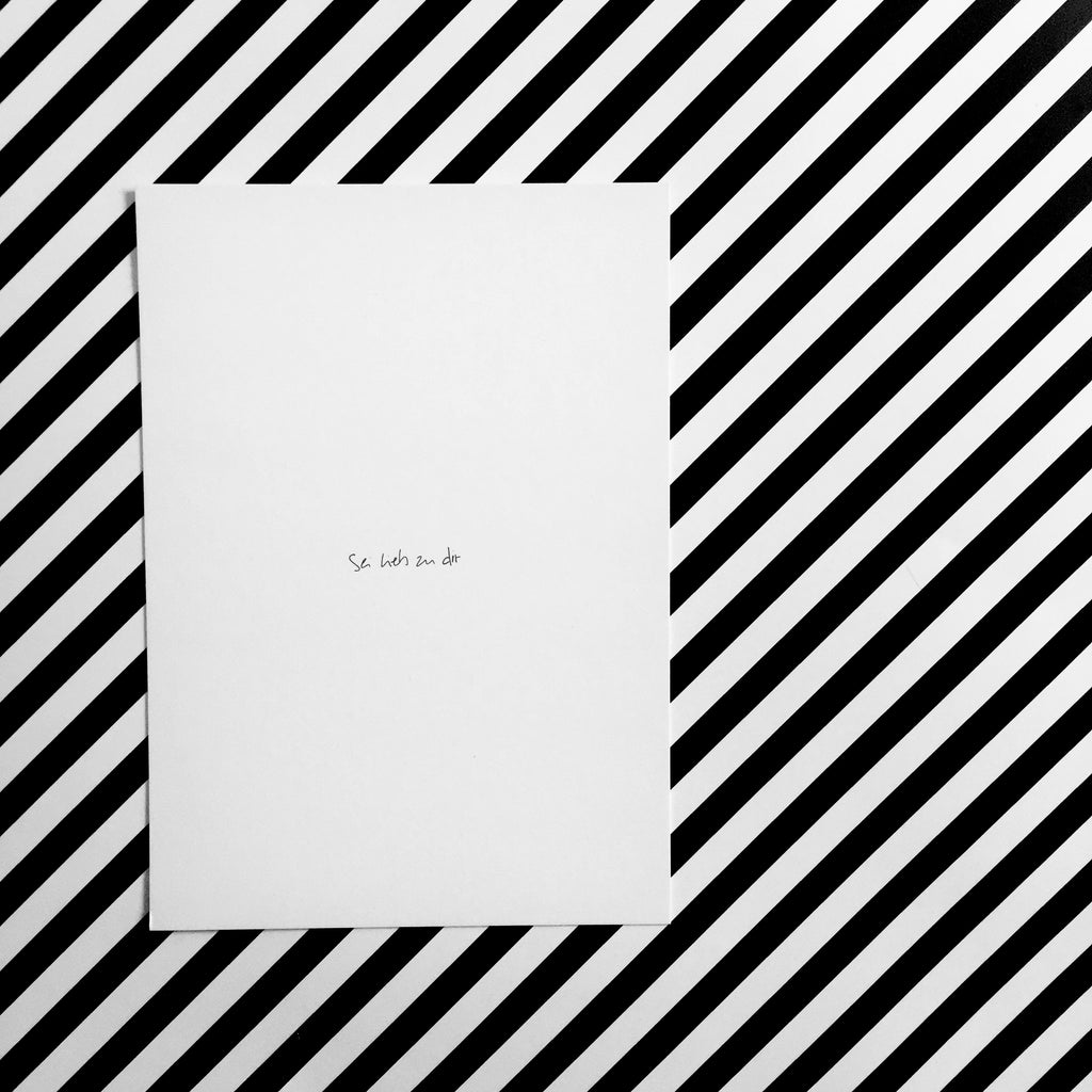 Weiße Postkarte mit schwarzer Schrift "Sei lieb zu dir"