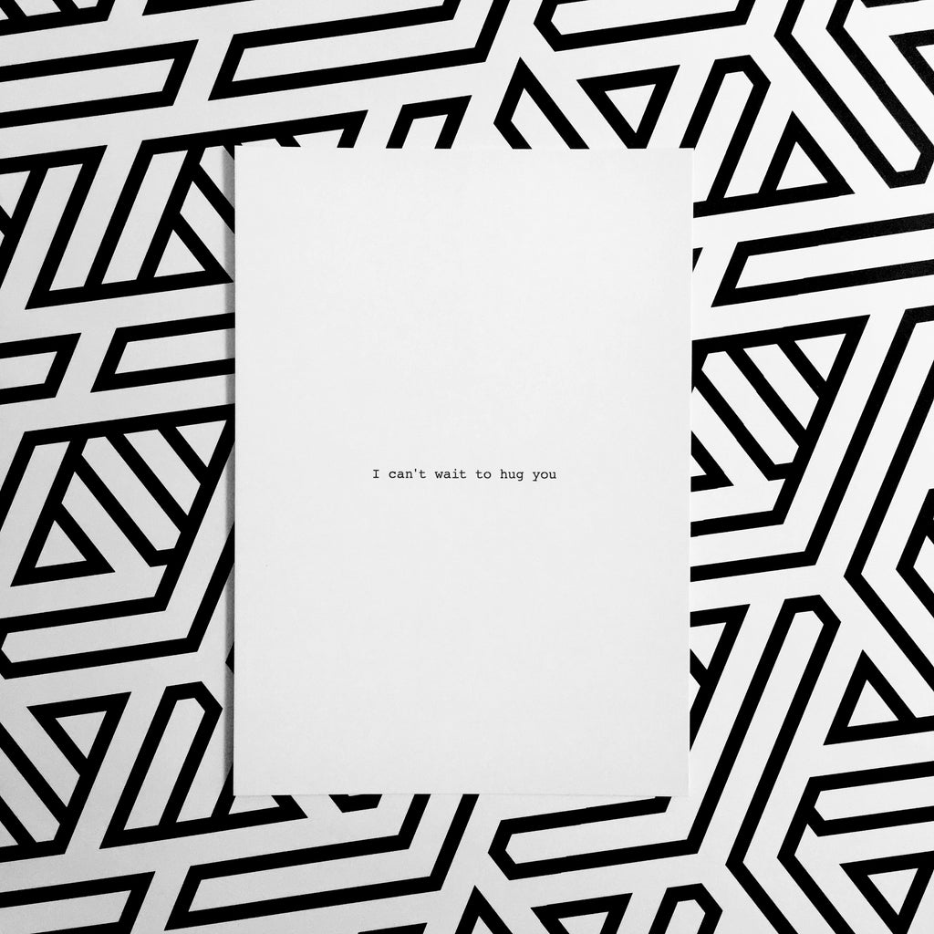Weiße Postkarte mit schwarzer Schrift "I can't  wait to hug you"