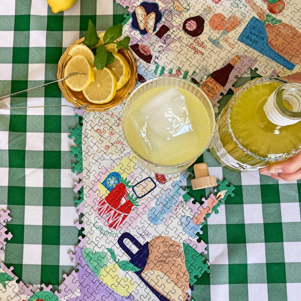 Amore Puzzle, teilweise gepuzzelt auf einer grün-weiß karierten Tischdecke mit Getränken und Zitronenscheiben
