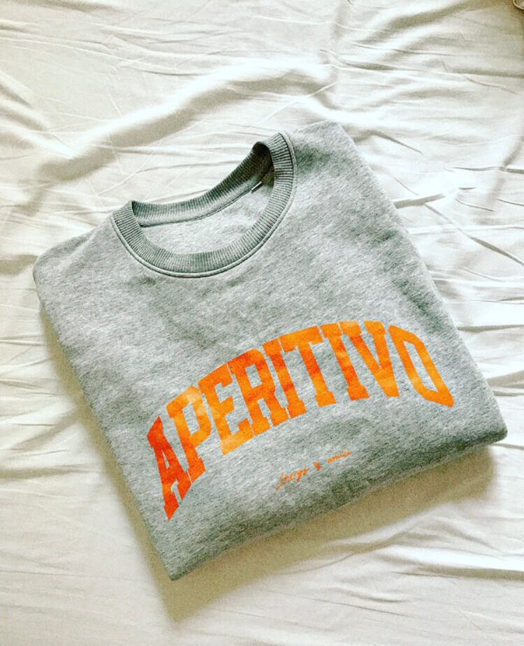 Graues Sweatshirt mit orangenem Schriftzug "Aperitivo" auf der Brust, im College-Style