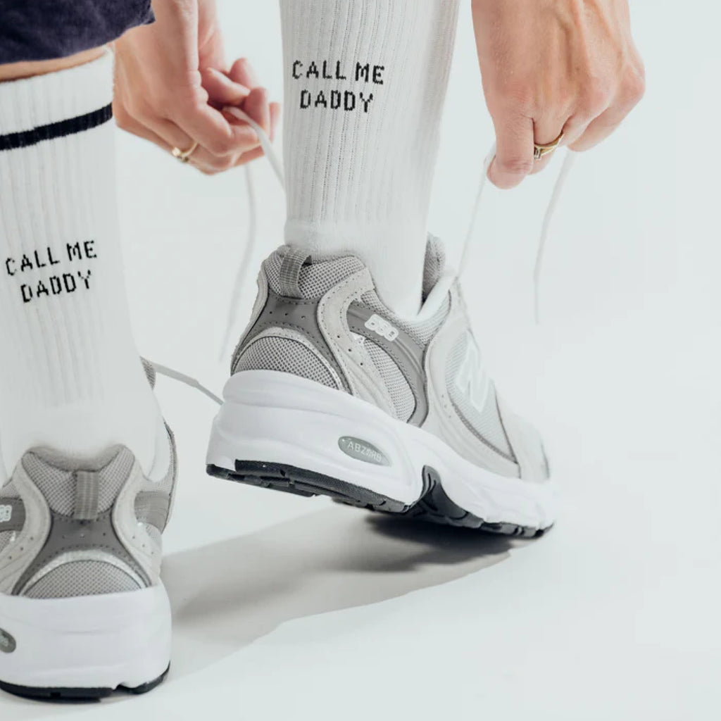Model trägt White Statement Socks mit Schriftzug: call me daddy und bindet sich die Schuhe