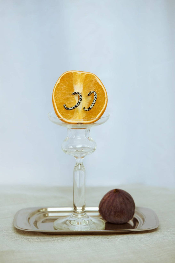 Loop Dott X Ohrringe auf einer Orangenscheibe mit Glas und Tablett