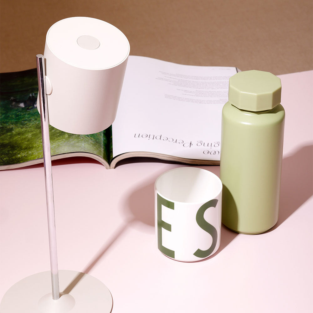 Designletter-Tasse mit Flasche, Lampe und Buch auf rosafarbenem Tisch