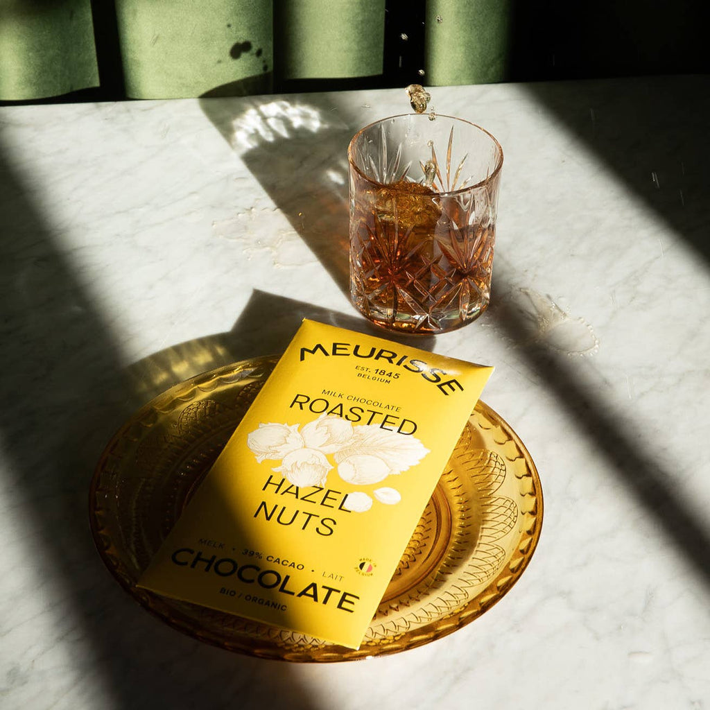 Bio-Milchschokolade mit gerösteten Haselnüssen auf einem Tisch mit einem Glas und einem Teller 