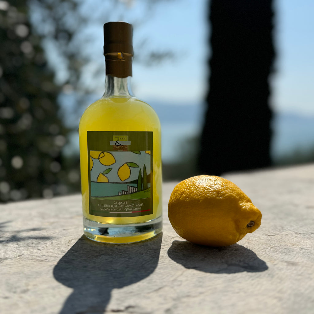 Limoncino und eine Zitrone auf einer Steinmauer, im Hintergrund der Gardasee