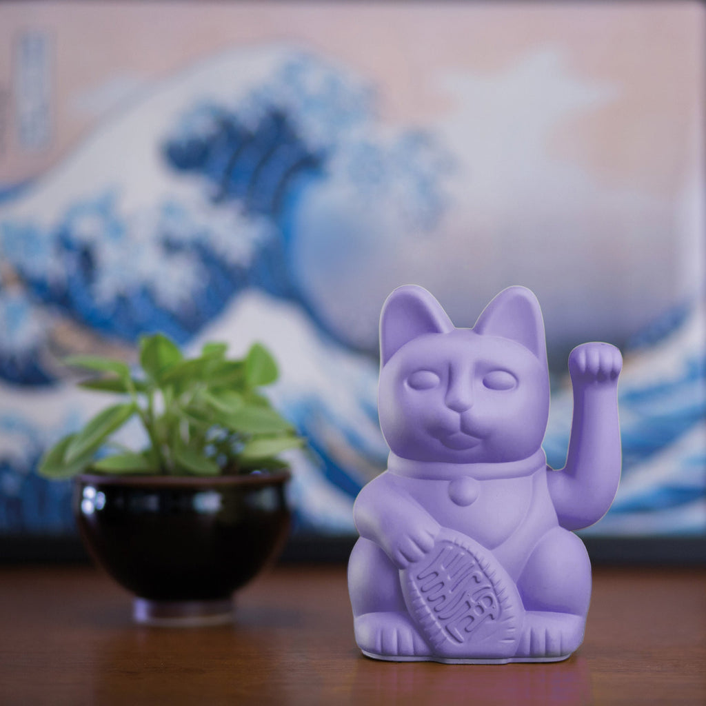 Lucky Cat lilac auf braunem Tisch mit einer kleinen Topfpflanze