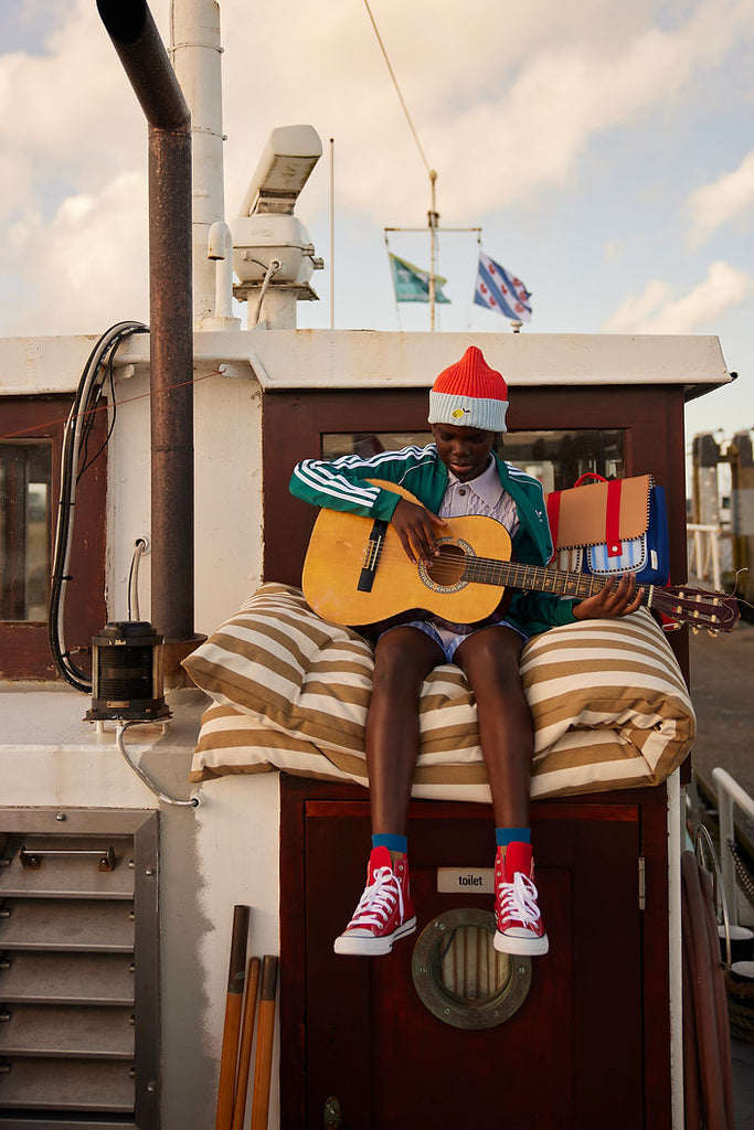 Rot & Hellblau X Beanie für Kinder, getragen von einem Kind mit Gitarre