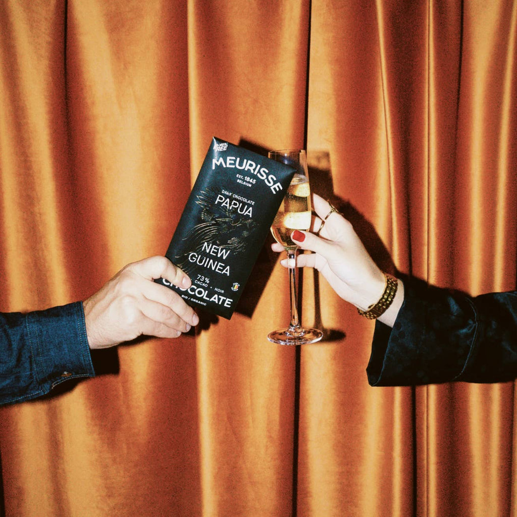 Dunkle Bio-Schokolade aus Papua-Neuguinea X Vegan mit Sektglas vor Vorhang 