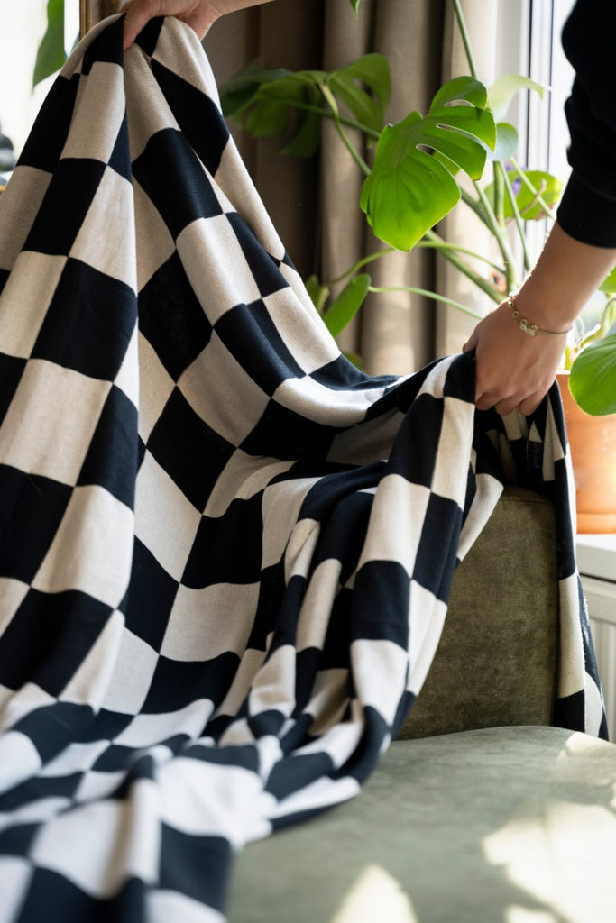 Ecru-Schwarz X Caro Plaid Kuscheldecke wird auf eine grüne Couch gelegt