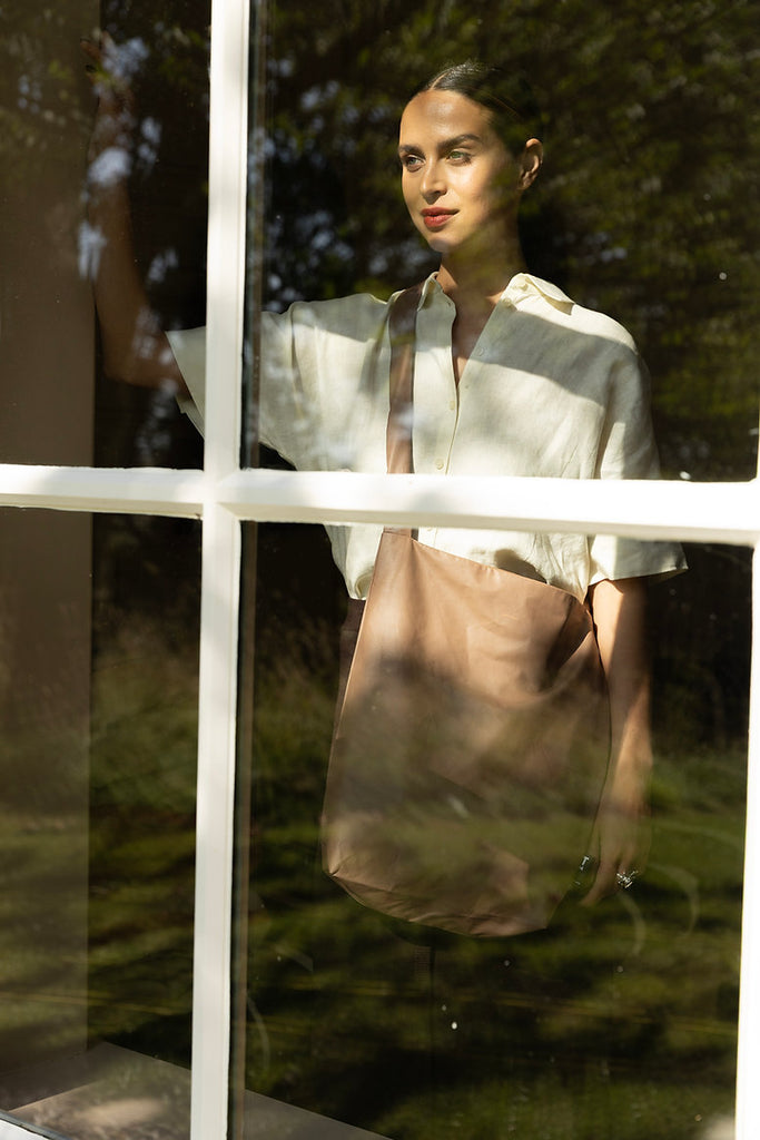 Beaver Fur X Feel Good Bag, von einem Model crossbody getragen, fotografiert durch ein Fenster