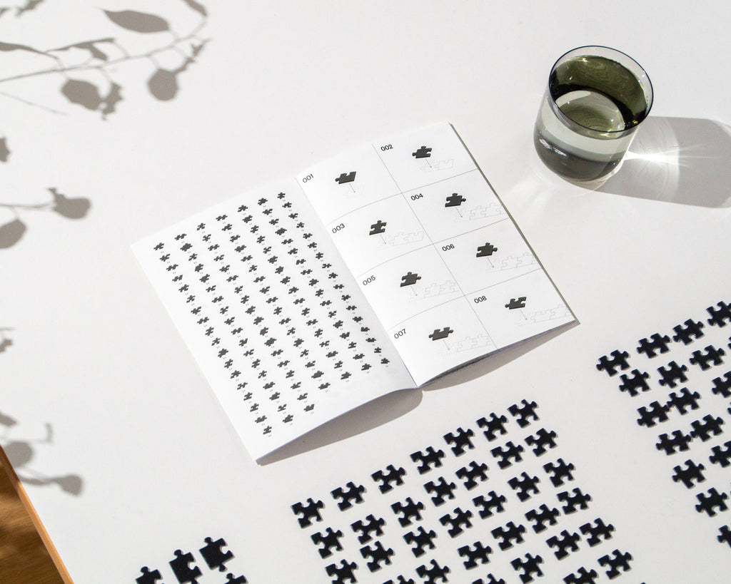 Demotivierendes Puzzle, Puzzleteile, Anleitung und ein Glas Wasser auf einem Tisch