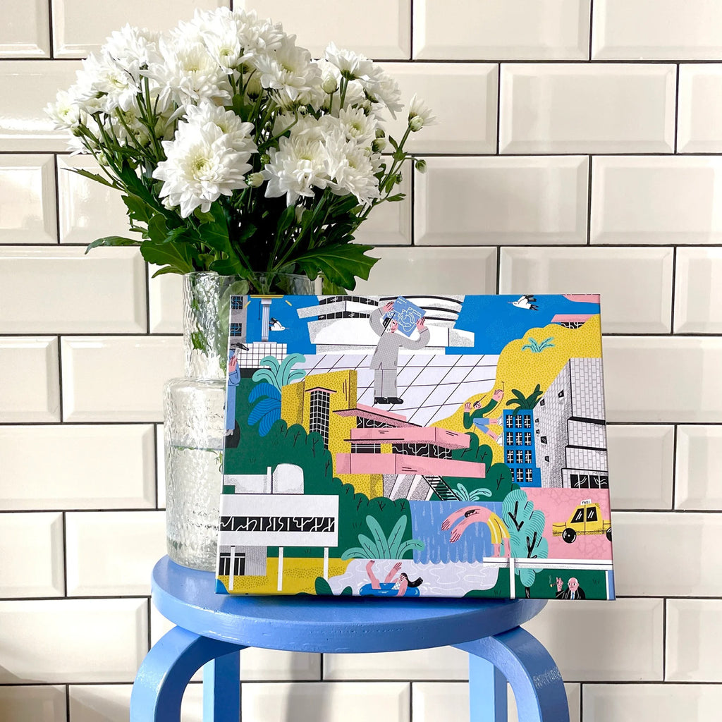 Architectural Masterpieces in Pieces, Verpackungskarton auf blauem Hocker, vor einer Blumenvase