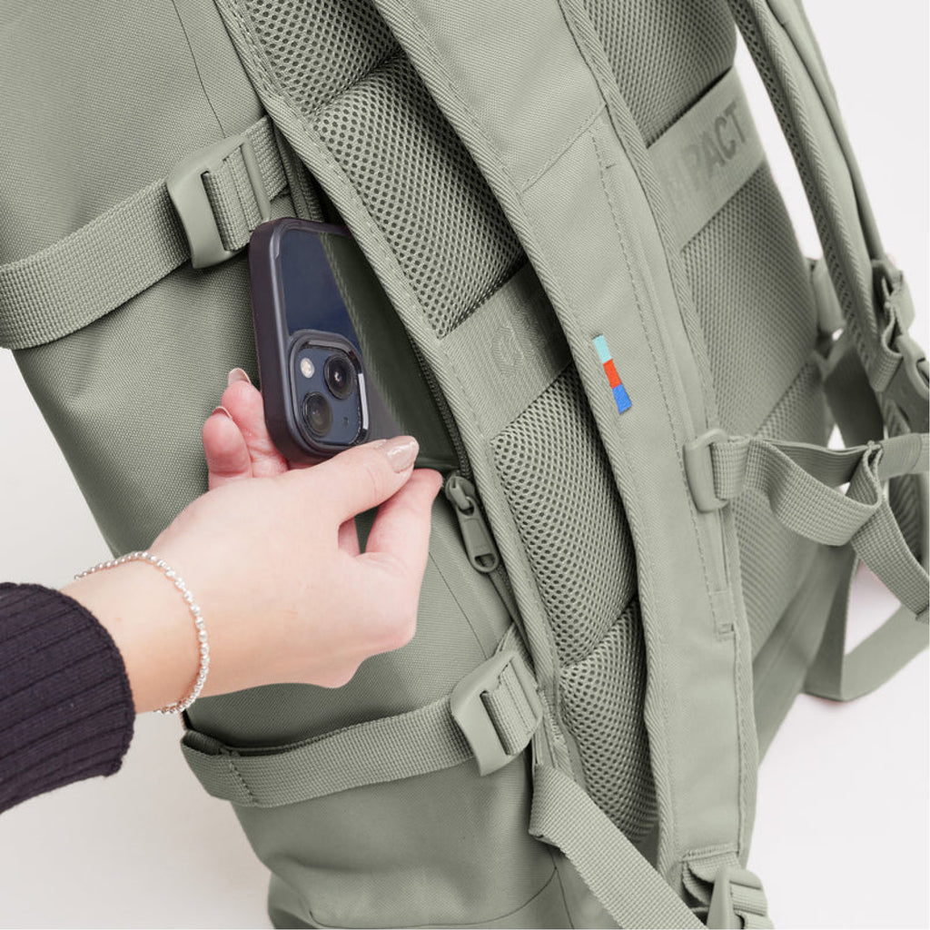 Rolltop 2.0 x Bass (hellgrün), ein Model steckt ein Handy in die versteckte Rückentasche