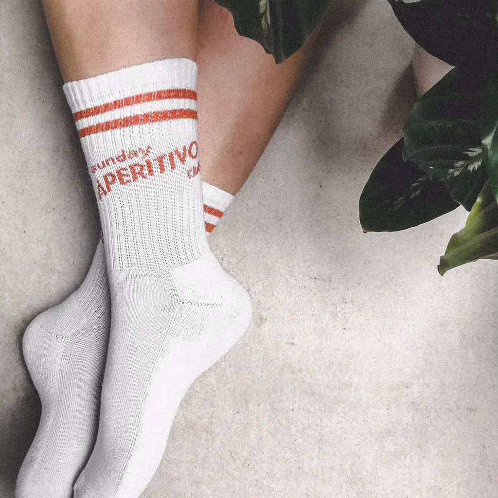 Weiße Tennis-Socken mit zwei orangenen Streifen und dem Schriftzug "sunday Aperitivo Club"