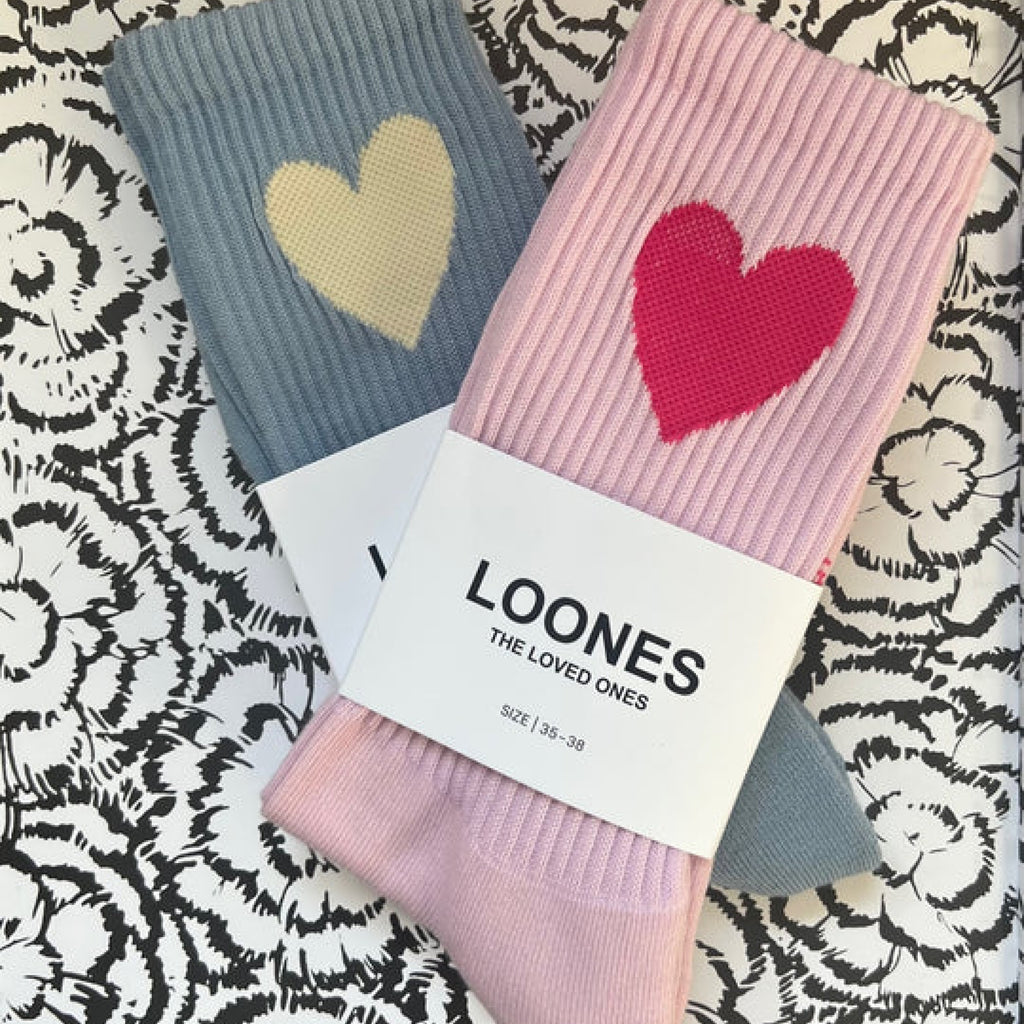 Big Heart X Lovely Socks, zwei Paar fotografiert auf einer Tischdecke. Rosa mit Herz in magenta-pink und graublau mit Herz in vanilla-white