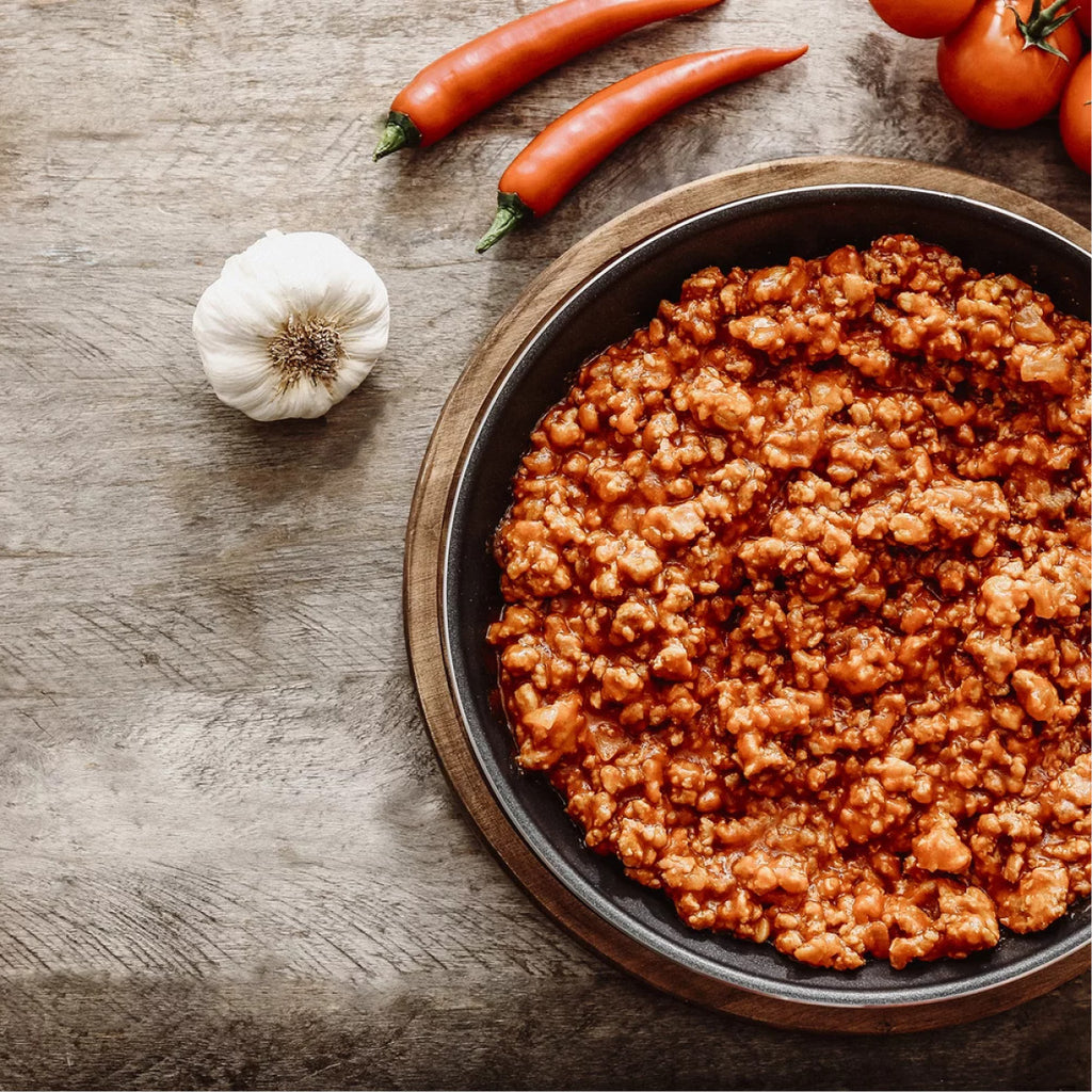 Eine Schüssel mit zubereitetem Hack, daneben, Tomaten, Peperoni, Knoblauch auf einem Holztisch